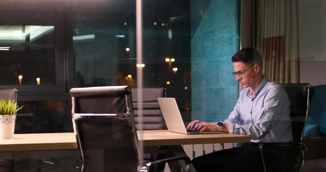 Young man working on laptop at night in dark office. The designer works in the later time.