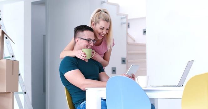 Young couple moving in a new home. Man and woman at the table using notebook laptop computer and plans with boxes around them