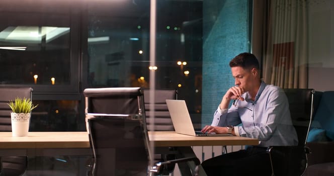 Young man working on laptop at night in dark office. The designer works in the later time.