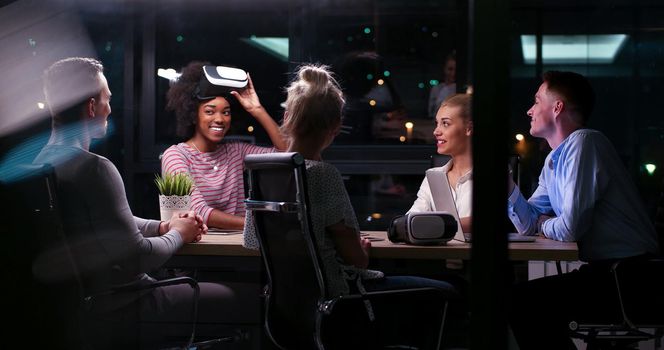 Multiethnic Business team using virtual reality headset in night office meeting  Developers meeting with virtual reality simulator around table in creative office.