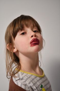 Cute little preschool girl playing with mommy's make up. Fashion experiment little child applying makeup lipstick and shadow on face, staying at home in corona virus quarantine.