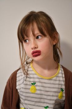 Cute little preschool girl playing with mommy's make up. Fashion experiment little child applying makeup lipstick and shadow on face, staying at home in corona virus quarantine.