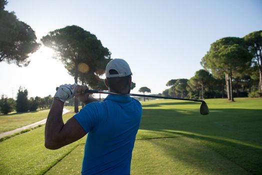 golf player hitting shot with club on course at beautiful morning with sun flare in background