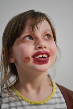 Cute little preschool girl playing with mommy's make up. Fashion experiment little child applying makeup lipstick and shadow on face, staying at home in corona virus quarantine.