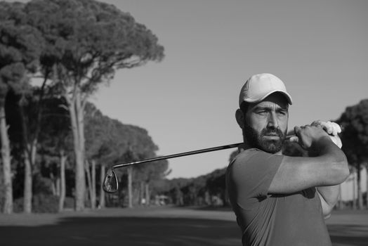 golf player hitting shot with club on course at beautiful morning with sun flare in background