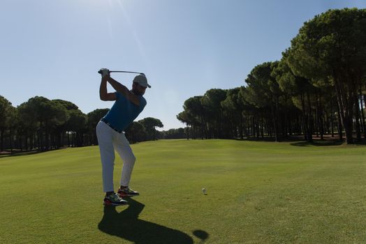 golf player hitting shot with club on course at beautiful morning with sun flare in background