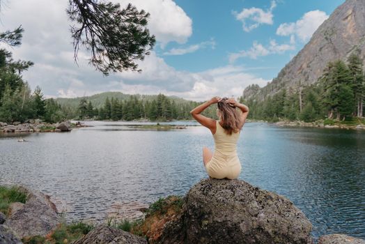 Tourist girl enjoys the magical view of the lake, coniferous forest and magical view sitting on big stone on the shore of a turquoise lake in the mountains. Hiking in the Natural Park. Black lake.