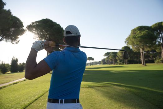 golf player hitting shot with club on course at beautiful morning with sun flare in background