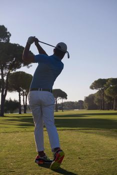 golf player hitting shot with club on course at beautiful morning with sun flare in background