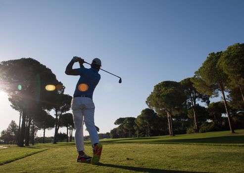 golf player hitting shot with club on course at beautiful morning with sun flare in background