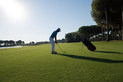 golf player hitting shot with club on course at beautiful morning with sun flare in background