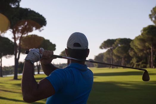 golf player hitting shot with club on course at beautiful morning with sun flare in background