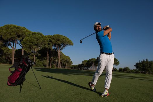 golf player hitting shot with club on course at beautiful morning with sun flare in background