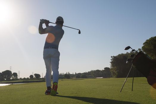 golf player hitting shot with club on course at beautiful morning with sun flare in background