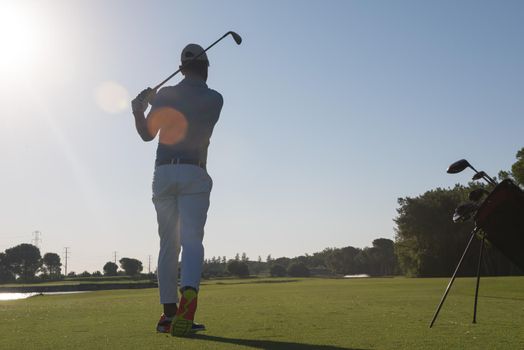 golf player hitting shot with club on course at beautiful morning with sun flare in background