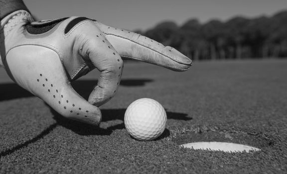 close up of man's hand putting golf ball in hole at course