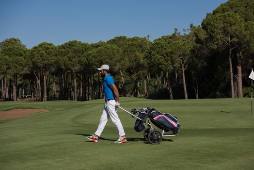 handsome middle eastern golf playerwalking with wheel bag at course on beautiful  sunny day