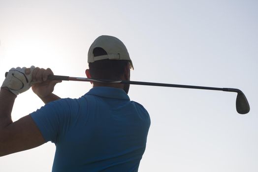 golf player hitting shot with club on course at beautiful morning with sun flare in background