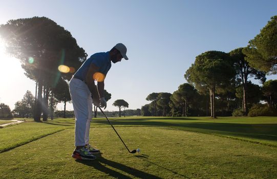 golf player hitting shot with club on course at beautiful morning with sun flare in background