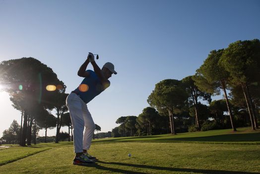 golf player hitting shot with club on course at beautiful morning with sun flare in background