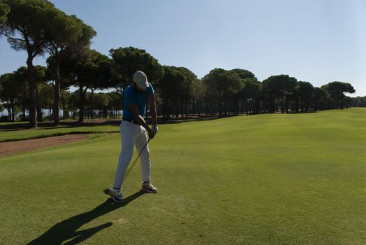 golf player hitting shot with club on course at beautiful morning with sun flare in background