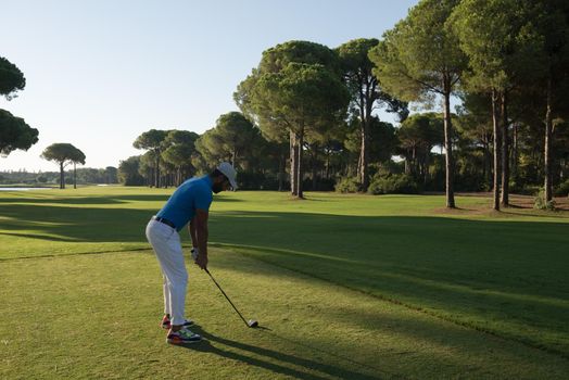 golf player hitting shot with club on course at beautiful morning with sun flare in background