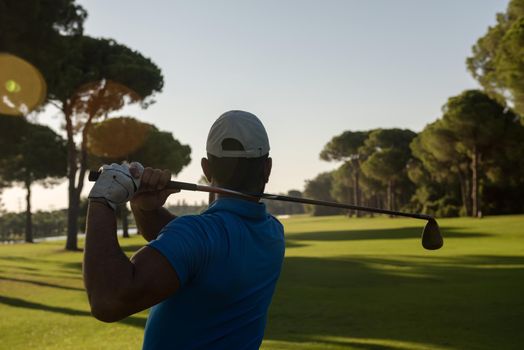 golf player hitting shot with club on course at beautiful morning with sun flare in background