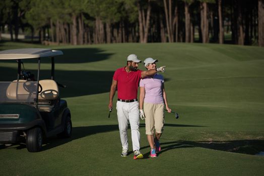 young couple walking to next hole on golf course. man carrying golf bag