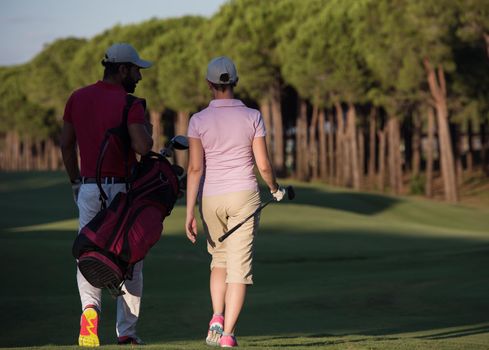 young couple walking to next hole on golf course. man carrying golf bag