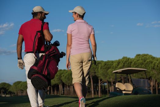 young couple walking to next hole on golf course. man carrying golf bag