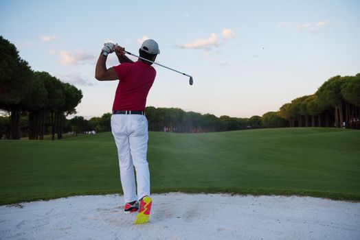 golf player shot ball from sand bunker at course with beautiful sunset with sun flare