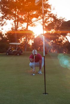 golf player aiming shot with club on course at beautiful sunset with sun flare in background