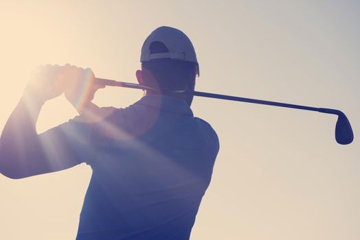 golf player hitting shot with club on course at beautiful morning with sun flare in background