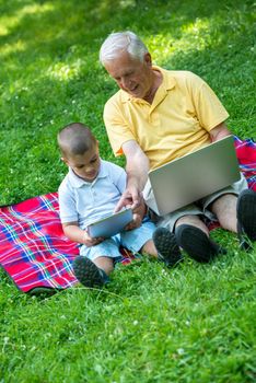 happy elderly senior grandfather and child in park using laptop computer