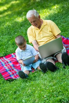 happy elderly senior grandfather and child in park using laptop computer