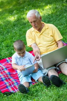 happy elderly senior grandfather and child in park using laptop computer