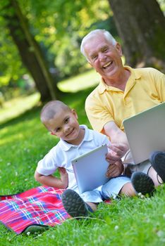 happy elderly senior grandfather and child in park using laptop computer