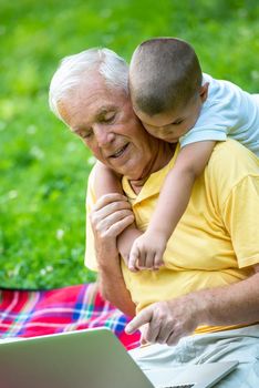 happy elderly senior grandfather and child in park using laptop computer