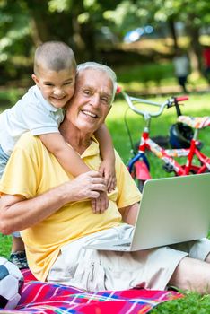 happy elderly senior grandfather and child in park using laptop computer