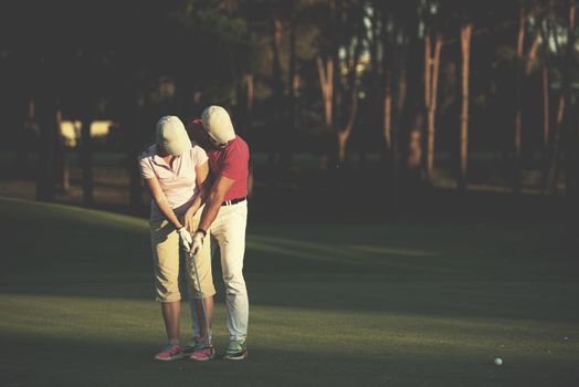 male golf instructor teaching female golf player, personal trainer giving lesson on golf course