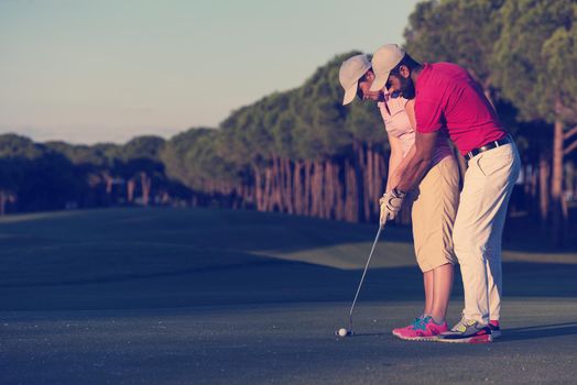 male golf instructor teaching female golf player, personal trainer giving lesson on golf course