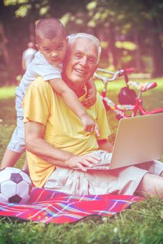 happy elderly senior grandfather and child in park using laptop computer