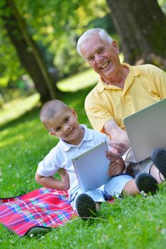 happy elderly senior grandfather and child in park using laptop computer