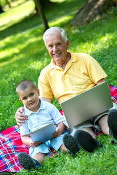 happy elderly senior grandfather and child in park using laptop computer