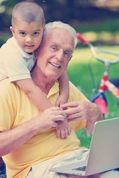 happy elderly senior grandfather and child in park using laptop computer