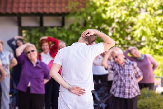 trainer training motivated active healthy senior people to performing exercise in the park