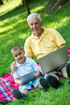 happy elderly senior grandfather and child in park using laptop computer