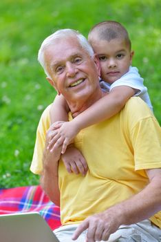 happy elderly senior grandfather and child in park using laptop computer