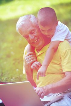 happy elderly senior grandfather and child in park using laptop computer