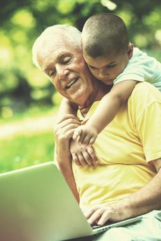 happy elderly senior grandfather and child in park using laptop computer